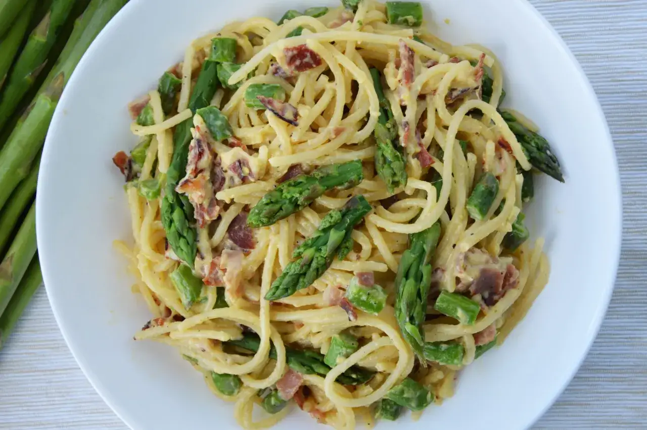 Pyszna carbonara ze szparagami, z chrupiącym boczkiem i kremowym sosem, podana na białym talerzu.