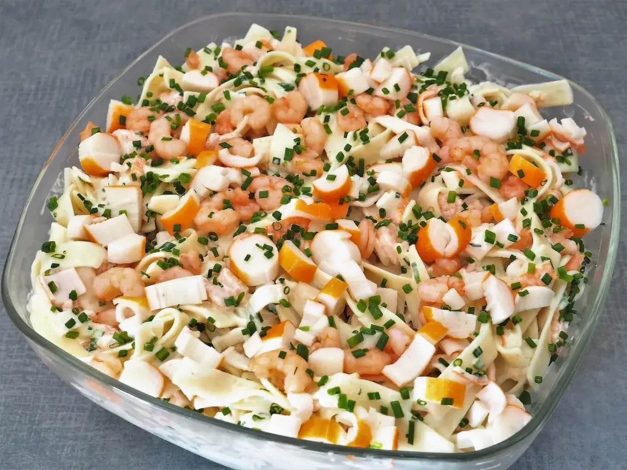 Salade Marco Polo : p&acirc;tes, crevettes, b&acirc;tonnets de surimi et ciboulette dans un plat en verre.