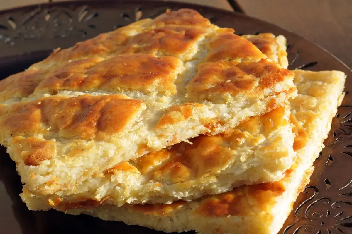 Une galette de pomme de terre dorée et croustillante, coupée en carrés et empilée sur une assiette décorative.