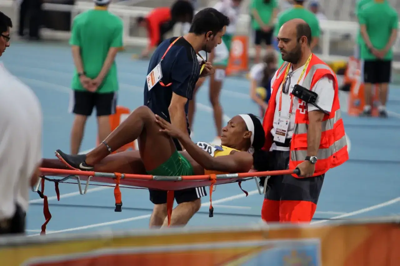 Na bieżni lekkoatletycznej ratownicy medyczni udzielają pomocy zawodniczce leżącej na noszach. To przykład szybkiej interwencji klinicznej medycyny sportowej.