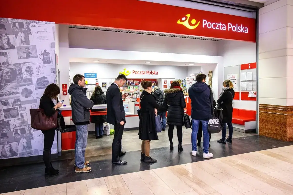 Kolejka do okienka Poczty Polskiej. Ludzie czekają na odbiór przesyłek, w tym na pocztę poste restante.