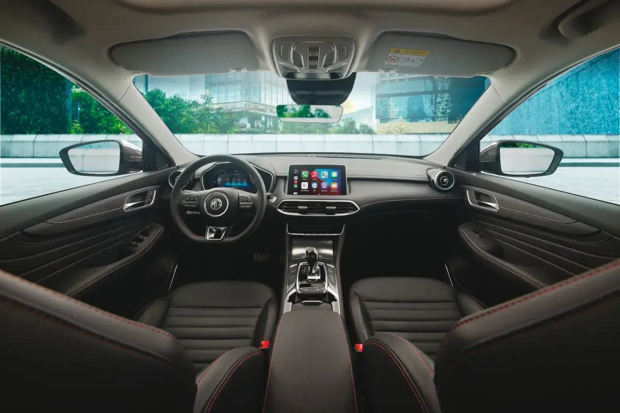 Interior del MG HS, con asientos de cuero negro y costuras rojas. El tablero muestra una pantalla t&aacute;ctil moderna y el volante multifunci&oacute;n.