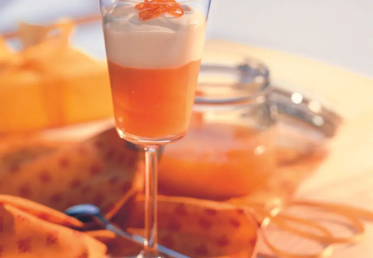 Ein Dessertglas mit orangefarbener Creme und Sahne, garniert mit kandierten Früchten. Die Gelatine-Verwendung sorgt für die perfekte Konsistenz.