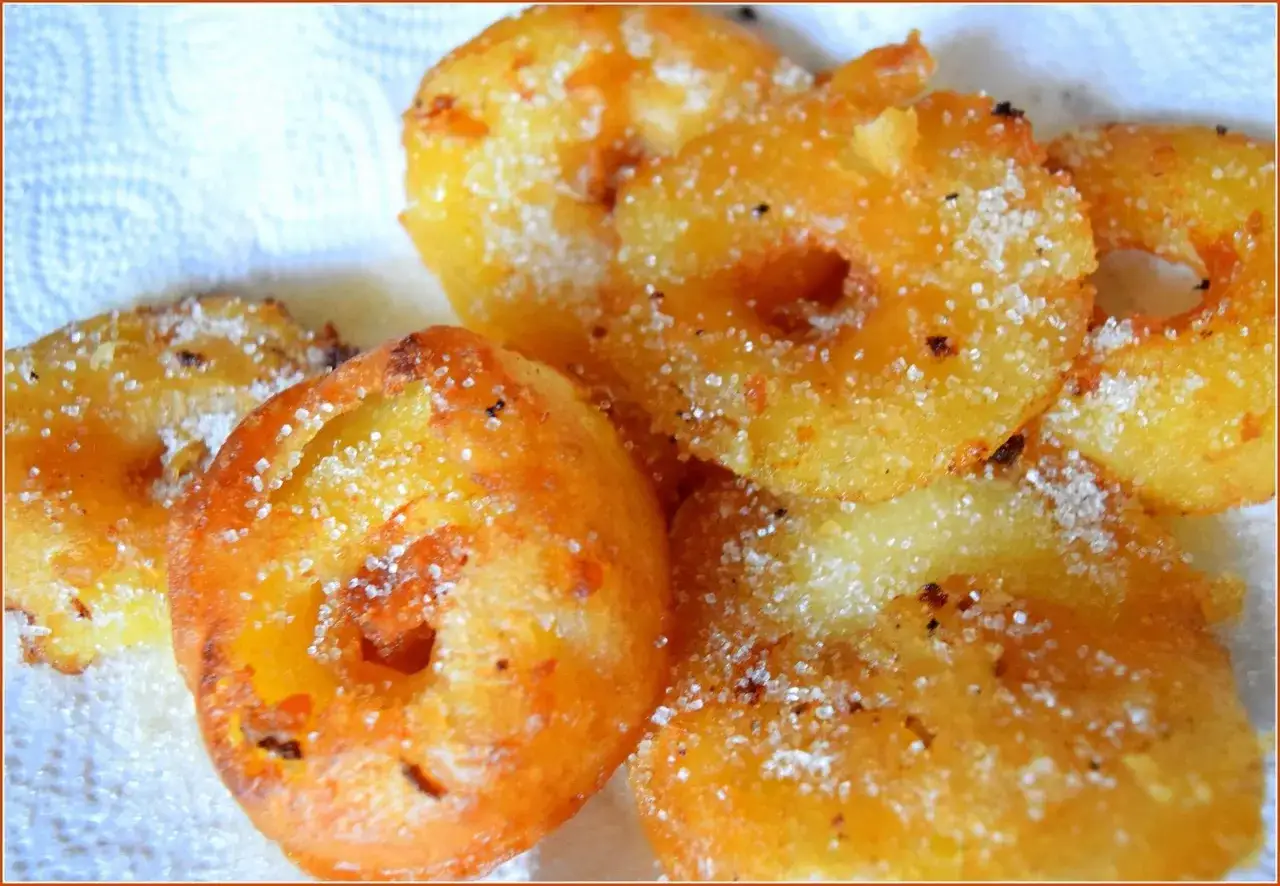 Des beignets aux pommes dorés et croustillants, saupoudrés de sucre, prêts à être dégustés.