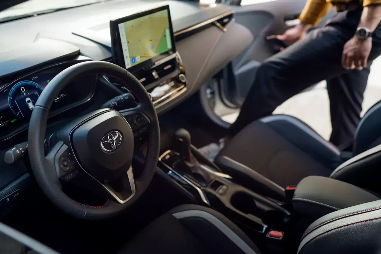 Wnętrze nowoczesnej corolli hybrid. Kierownica, ekran nawigacji i siedzenia. Mężczyzna wsiada do auta.