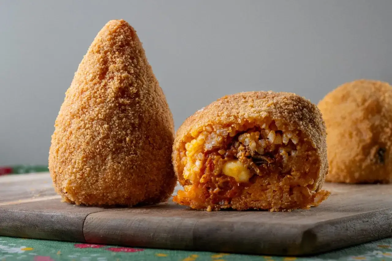 Arancino o arancina dorato e croccante, uno intero a forma di cono, l'altro tagliato a metà rivelando un ripieno saporito.