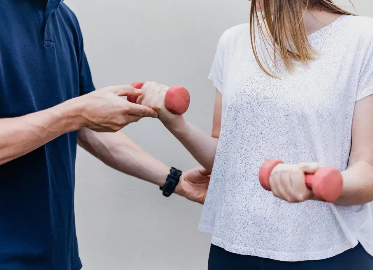 Therapeut unterstützt Patientin bei der Mobilisierung des Ellenbogens nach OP mit leichten Hanteln.