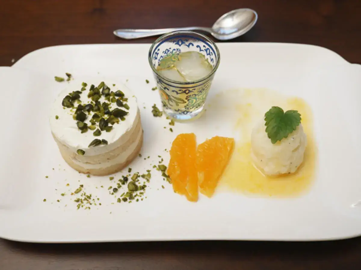 Ein Zitronen Tiramisu-Dessert mit Pistazien, Orangenspalten und einem Eisw&uuml;rfel-Drink.