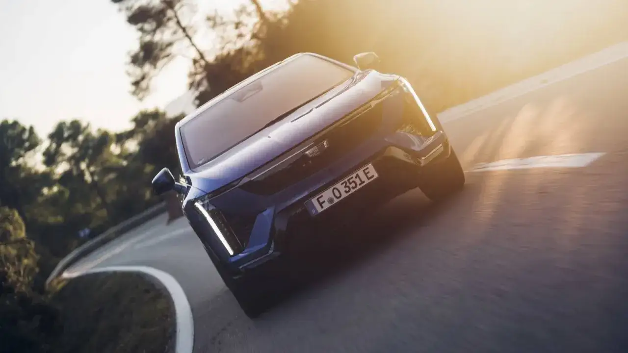 Un Cadillac azul el&eacute;ctrico, una de las marcas americanas de coches, serpentea por una carretera al atardecer.