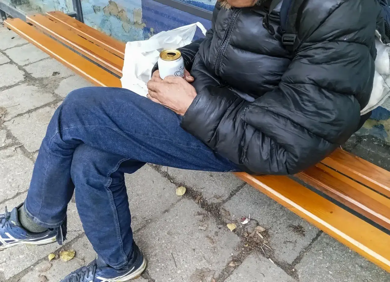 Osoba siedzi na ławce, trzymając puszkę. Zastanawia się, renta alkoholowa ile wynosi.