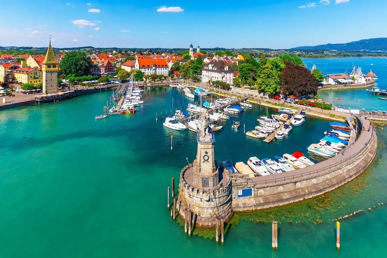 Malowniczy port nad Jeziorem Bodenskim, z łodziami, latarnią morską i kolorowymi budynkami w tle.