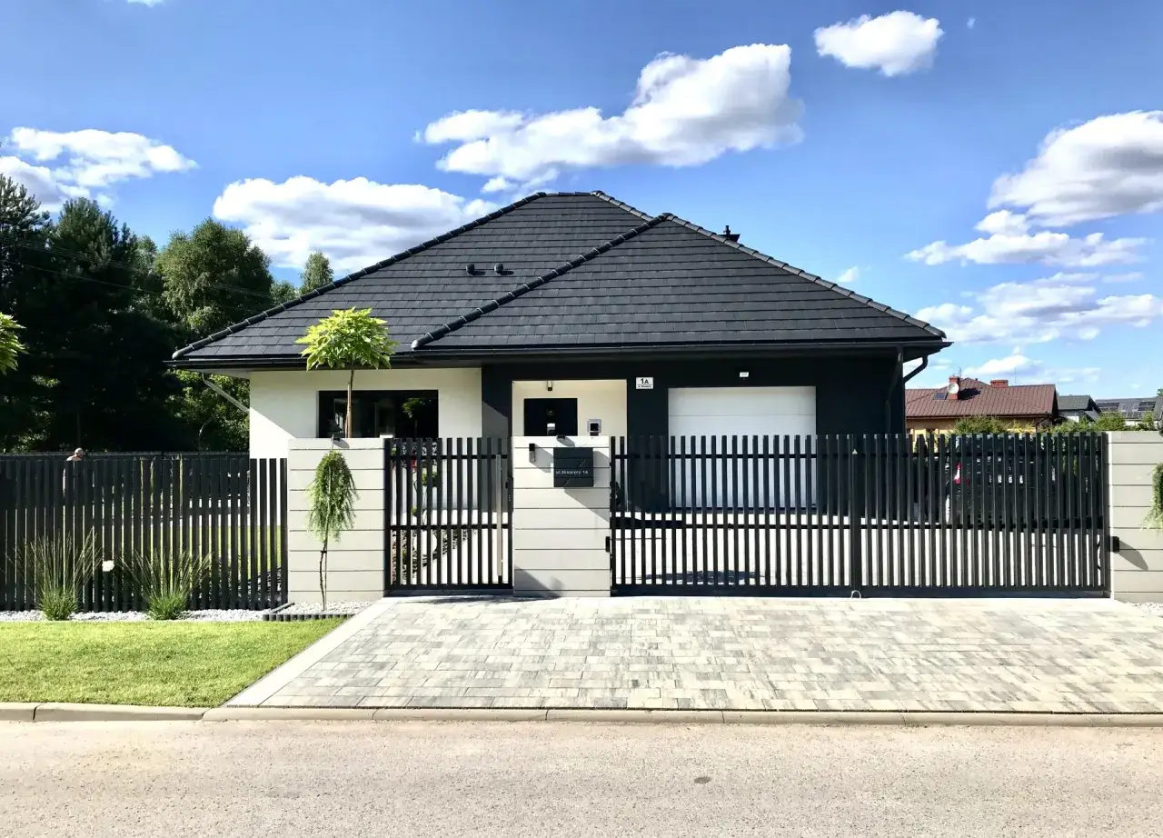Nowoczesny dom z czarnym, pionowym ogrodzeniem. Różne rodzaje ogrodzeń tworzą spójną całość z architekturą posesji.