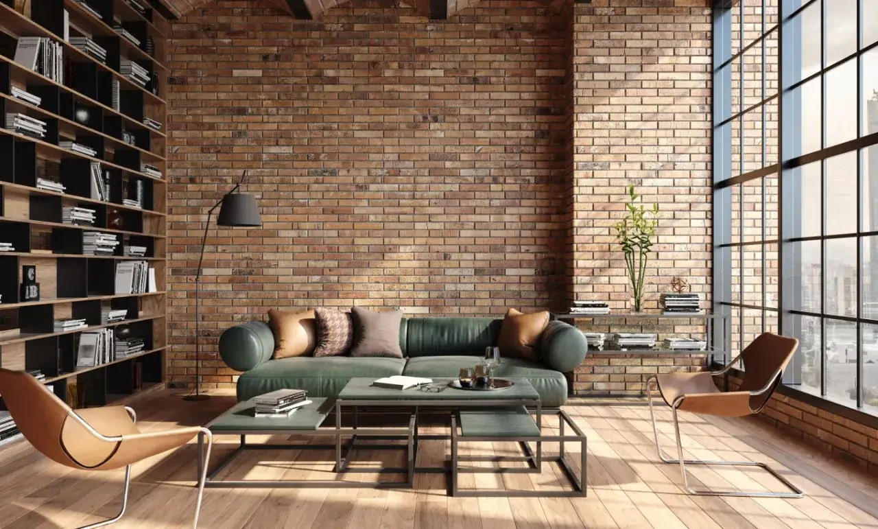 Wnętrze w **stylu loftowym**: zielona sofa, sk&oacute;rzane fotele, regały z książkami i ceglana ściana tworzą przytulną atmosferę.