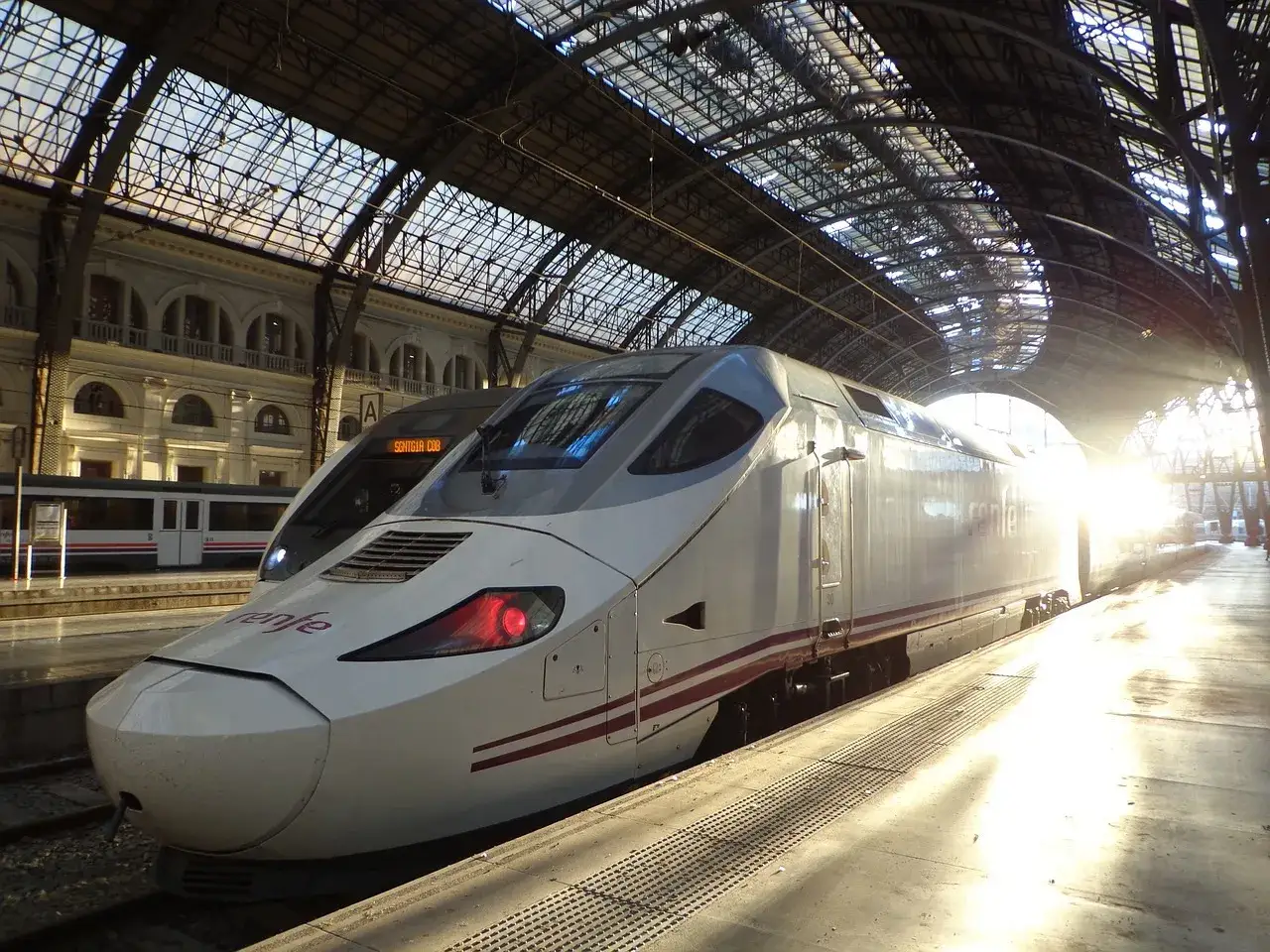Nowoczesny pociąg TGV Renfe na dworcu, oświetlony promieniami słońca przebijającymi przez szklany dach.
