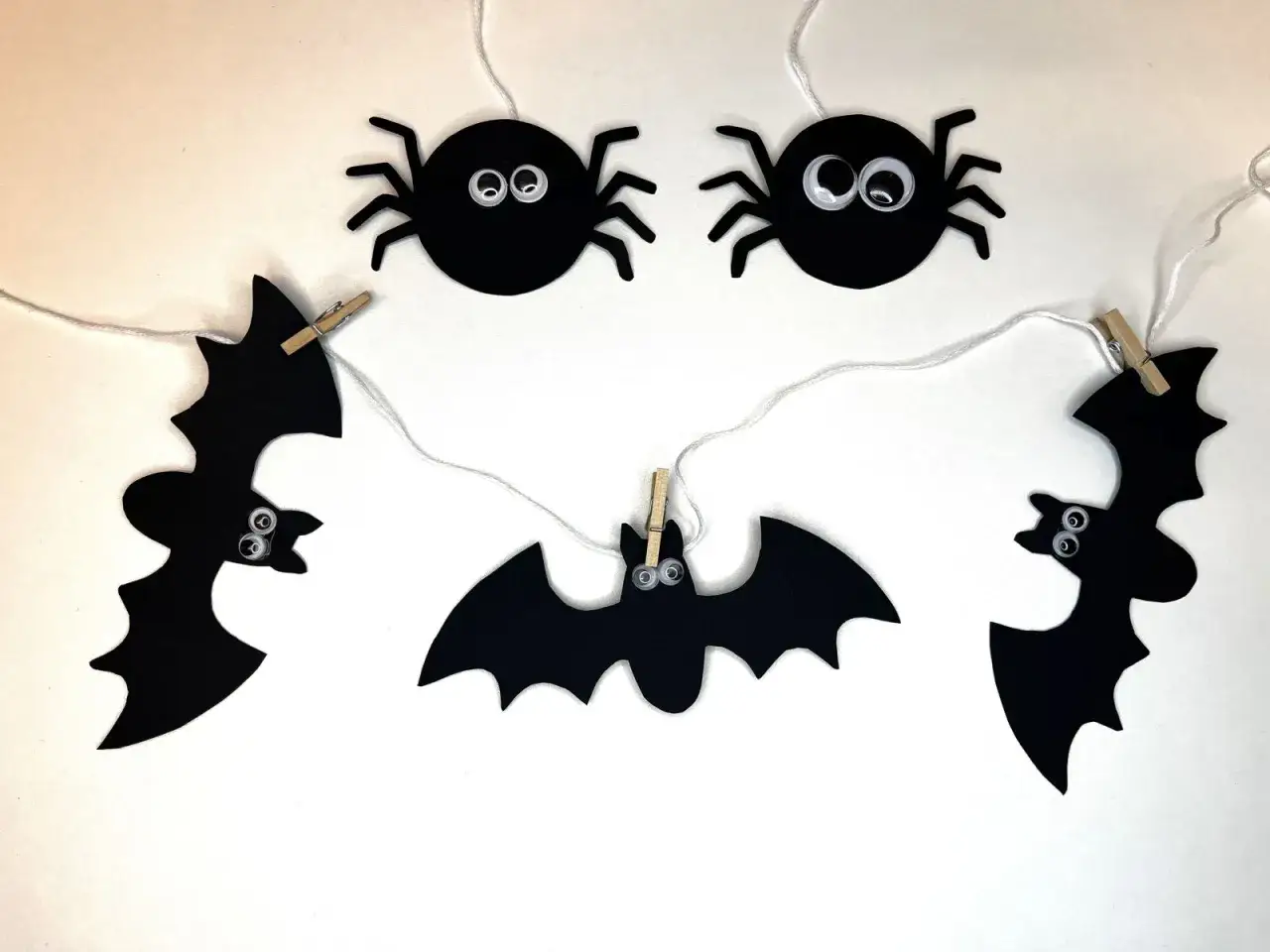 Söta fladdermöss och spindlar hänger på en tråd, redo att pyssla halloween.
