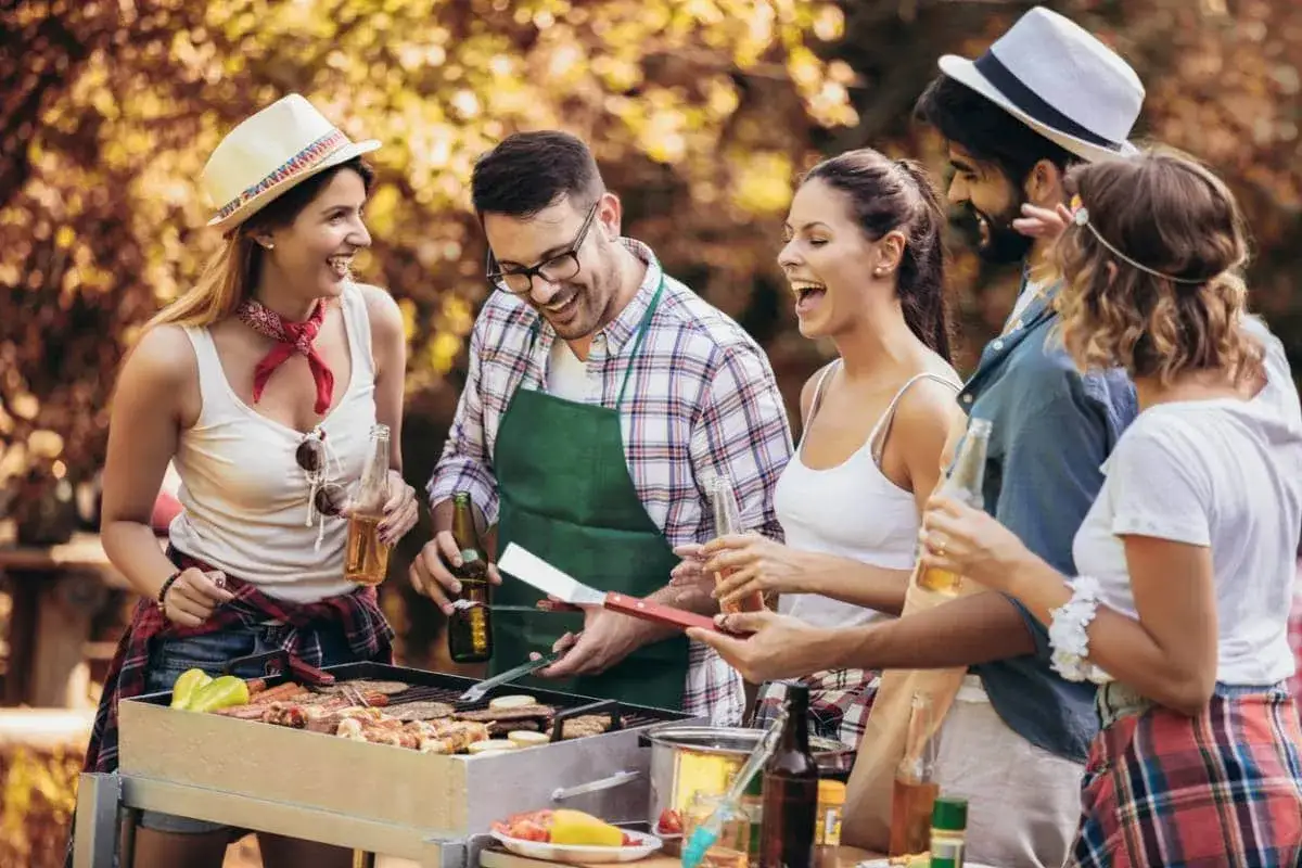 Amis riant autour d'un barbecue de Noël en plein air, avec des brochettes et des boissons.