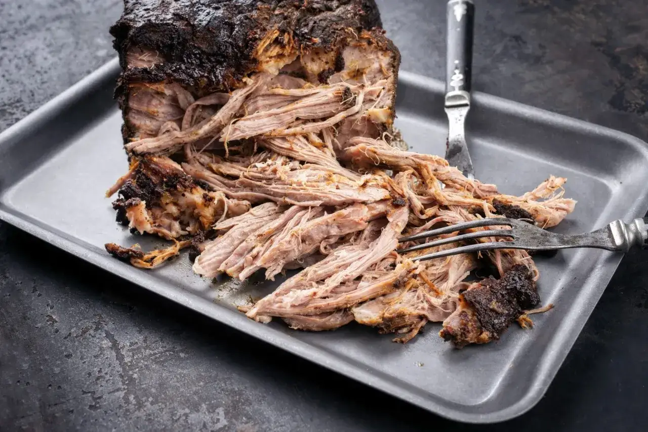 En stor bit pulled pork, tillagad i 12 timmar, ligger på en plåt. Köttet är mört och faller isär, redo att serveras.