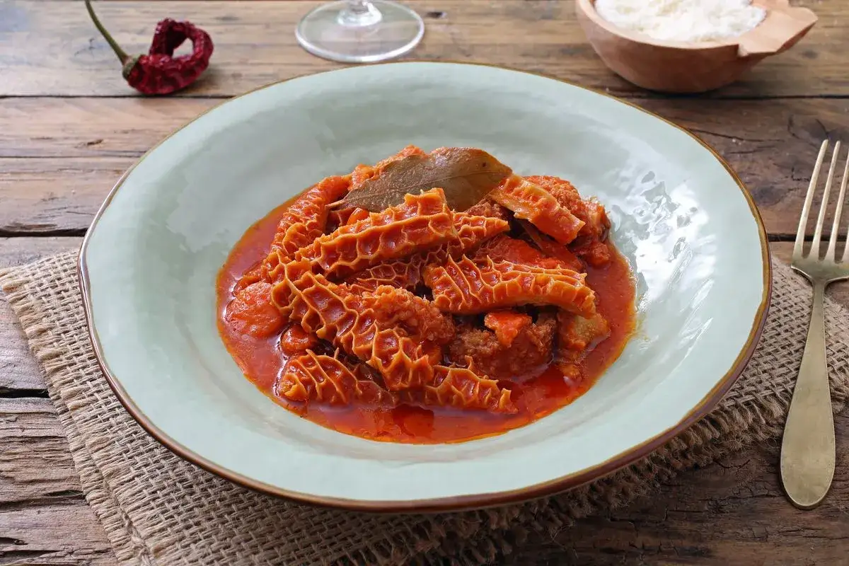 Piatto di trippa alla fiorentina fumante, con pomodoro e alloro, su un tavolo rustico.