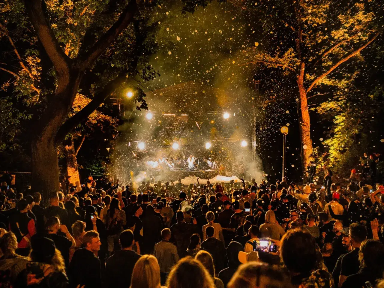 Tłum ludzi na koncercie pod gołym niebem, w powietrzu latają bańki mydlane. W tle scena z artystami, oświetlona reflektorami. Atmosfera jak na Audioriver 2026.