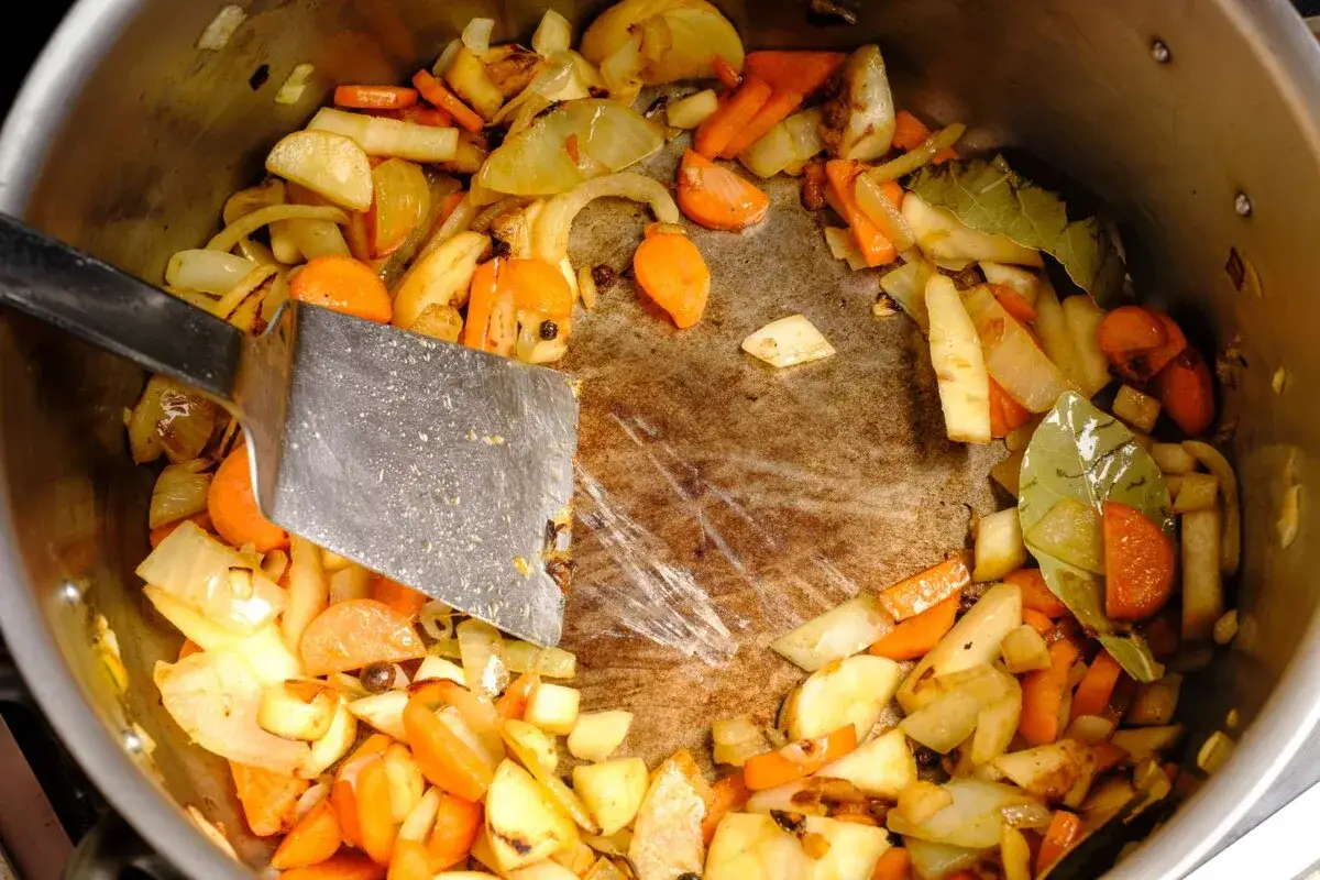 Gem&uuml;se wird in einem Topf angebraten, bereit f&uuml;r eine herzhafte braune Sauce. Ein Spachtel r&uuml;hrt die Karotten, Zwiebeln und Kartoffeln um.