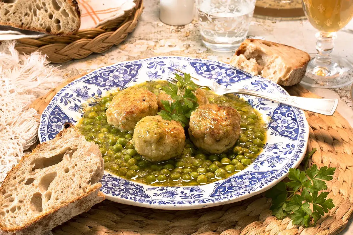 Albondigas de merluza en salsa verde con guisantes, acompañadas de pan rústico.