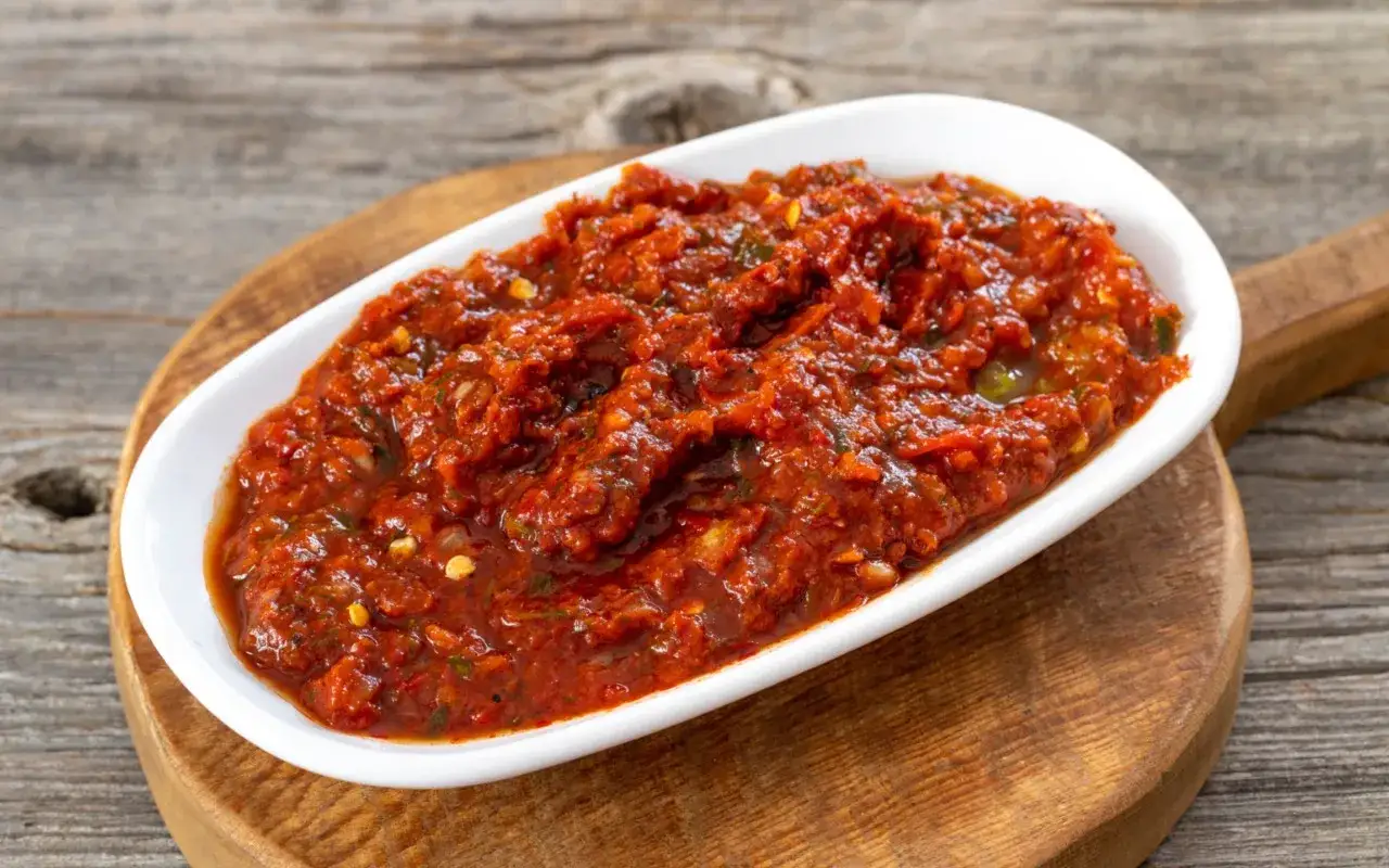 W&uuml;rziges Acili Ezme, eine scharfe Tomaten-Paprika-Paste, serviert in einer wei&szlig;en Schale auf einem Holzbrett.