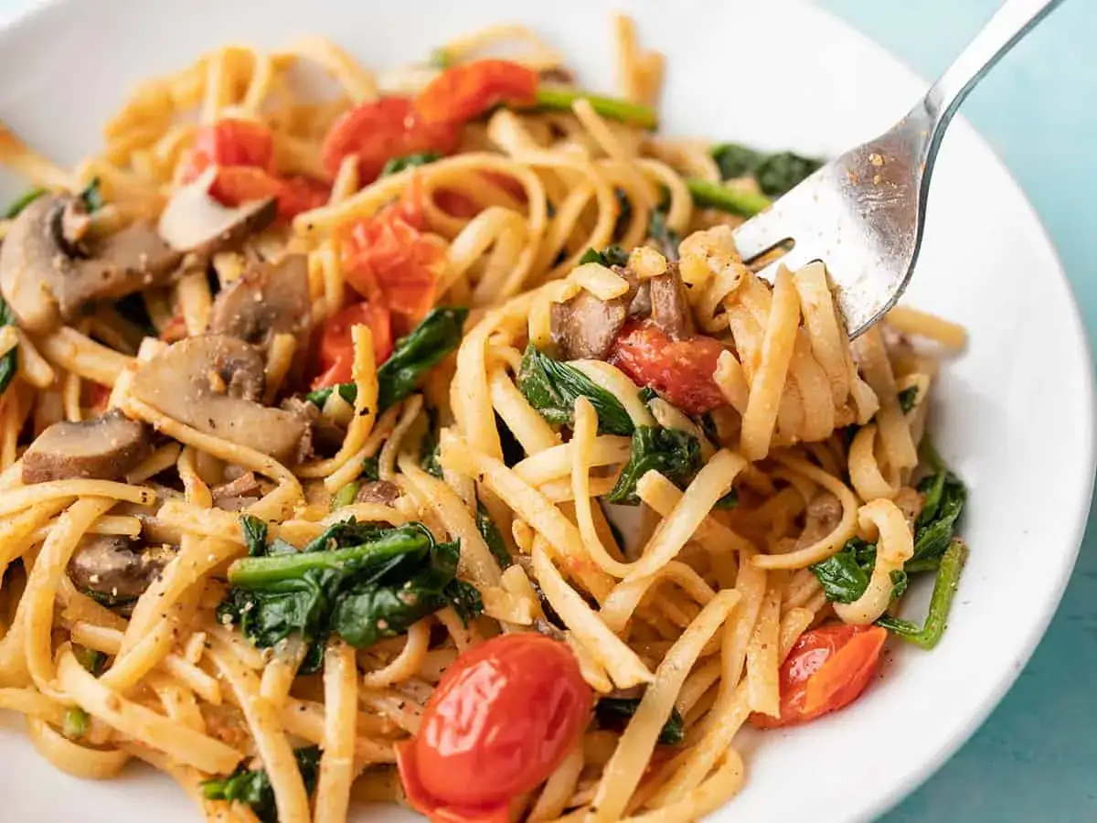 Gabel hebt Nudeln mit Pilzen, Spinat und Tomaten. Sind Nudeln gesund? Ja, mit viel Gemüse!