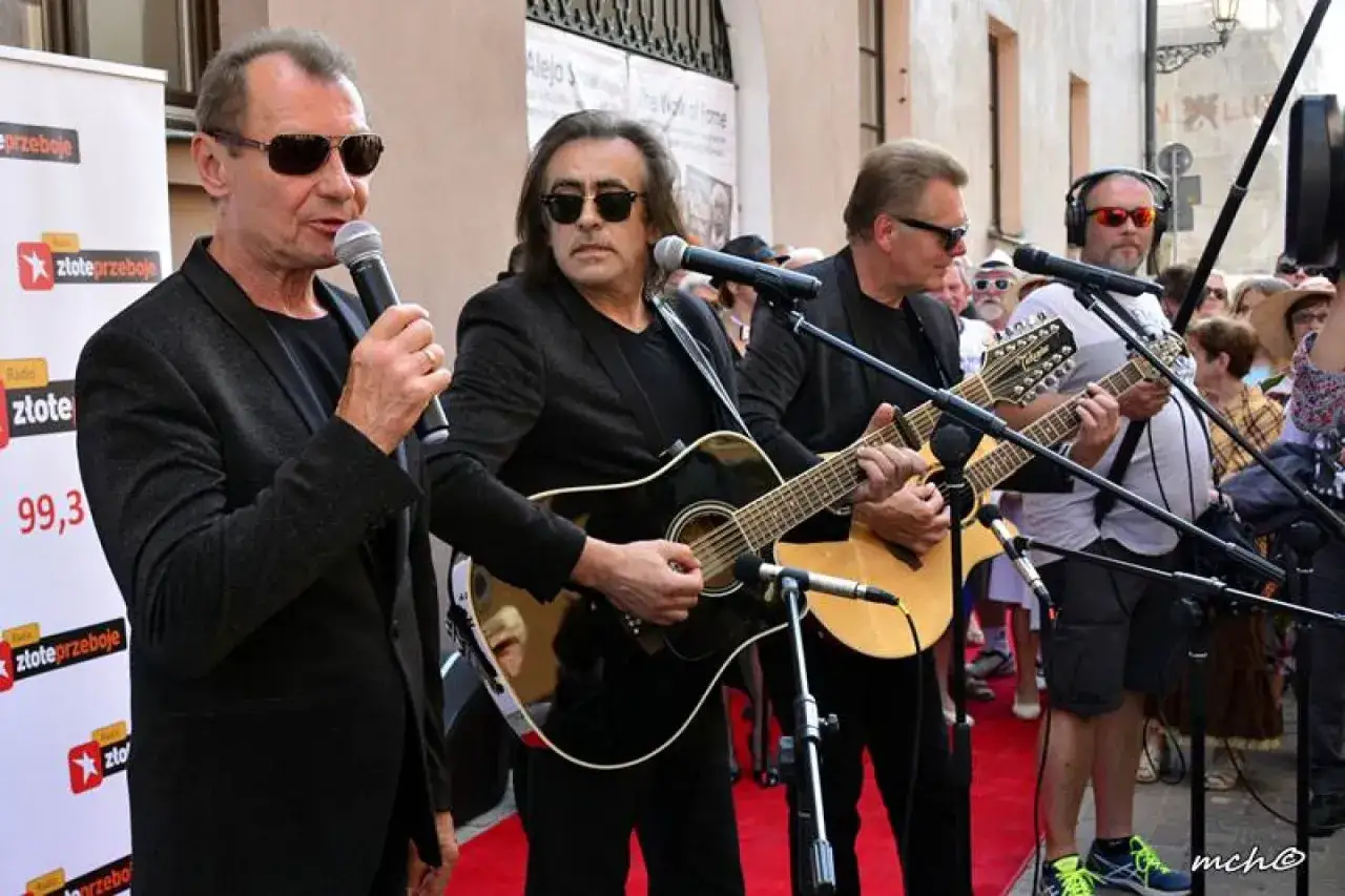 Zespół gra na gitarach, jeden z nich śpiewa do mikrofonu. To vox piosenki alfabetycznie.