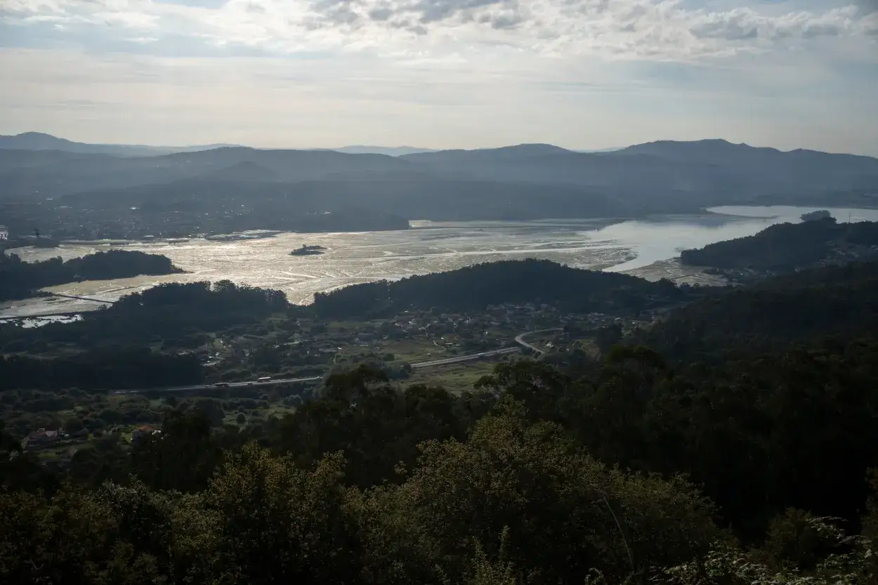 Vista panorámica del lago Castiñeiras con montañas al fondo y vegetación frondosa en primer plano.