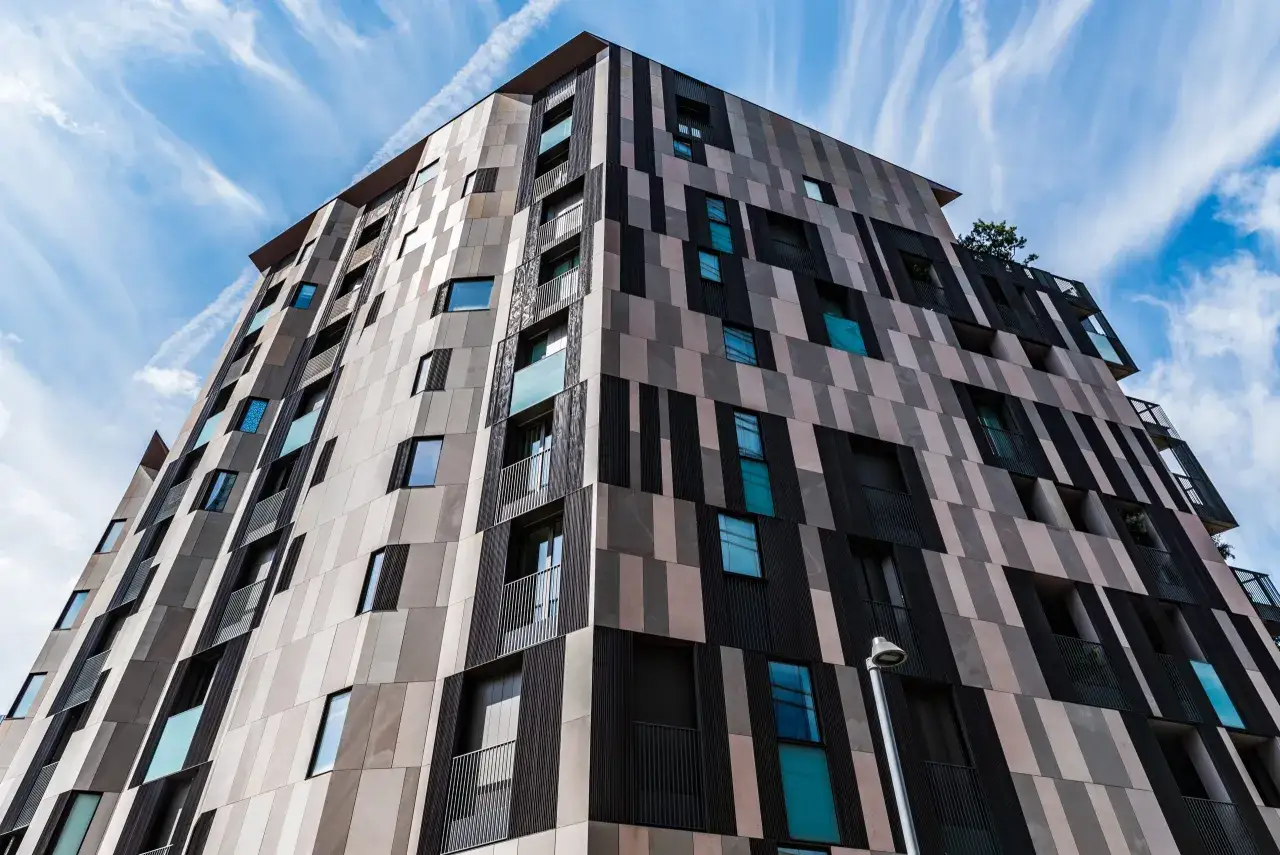 Edificio moderno con paredes de porcel&aacute;nico para fachadas exteriores, creando un patr&oacute;n geom&eacute;trico de colores y texturas bajo un cielo azul con nubes.