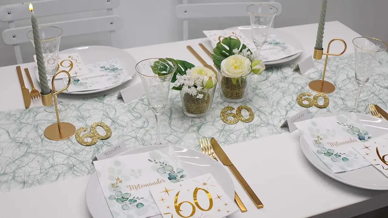 Festlich gedeckter Tisch für eine 60. Geburtstagsfeier. Goldene Kerzenhalter, Gläser und Besteck. Kleine Blumenarrangements und