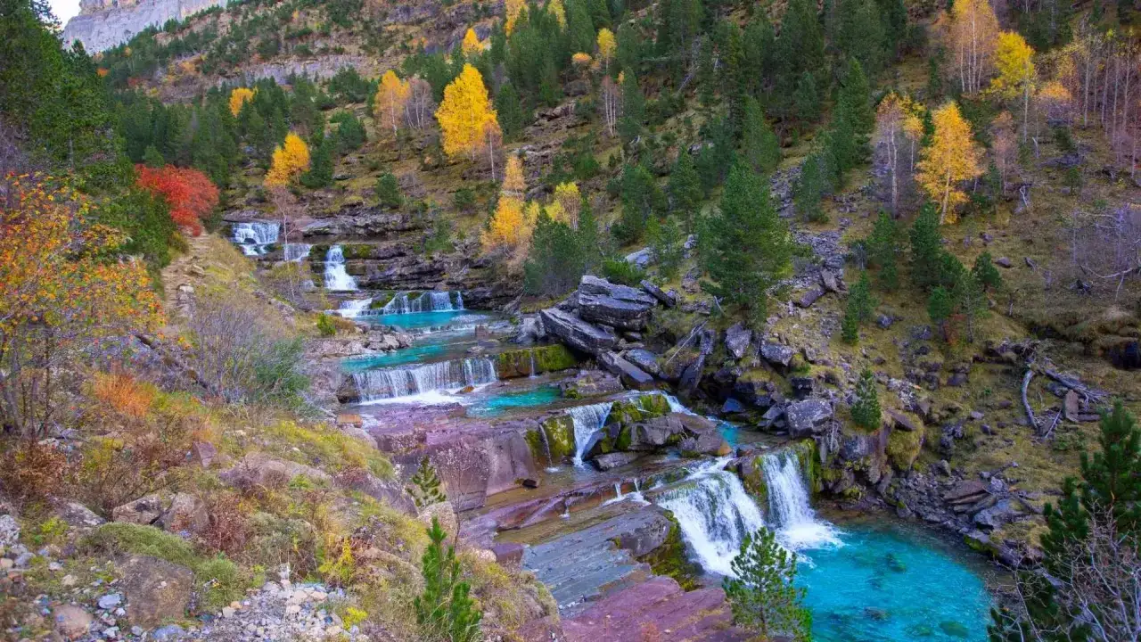 Cascada en la ruta Cola de Caballo, con aguas turquesas y vegetación otoñal en las laderas.