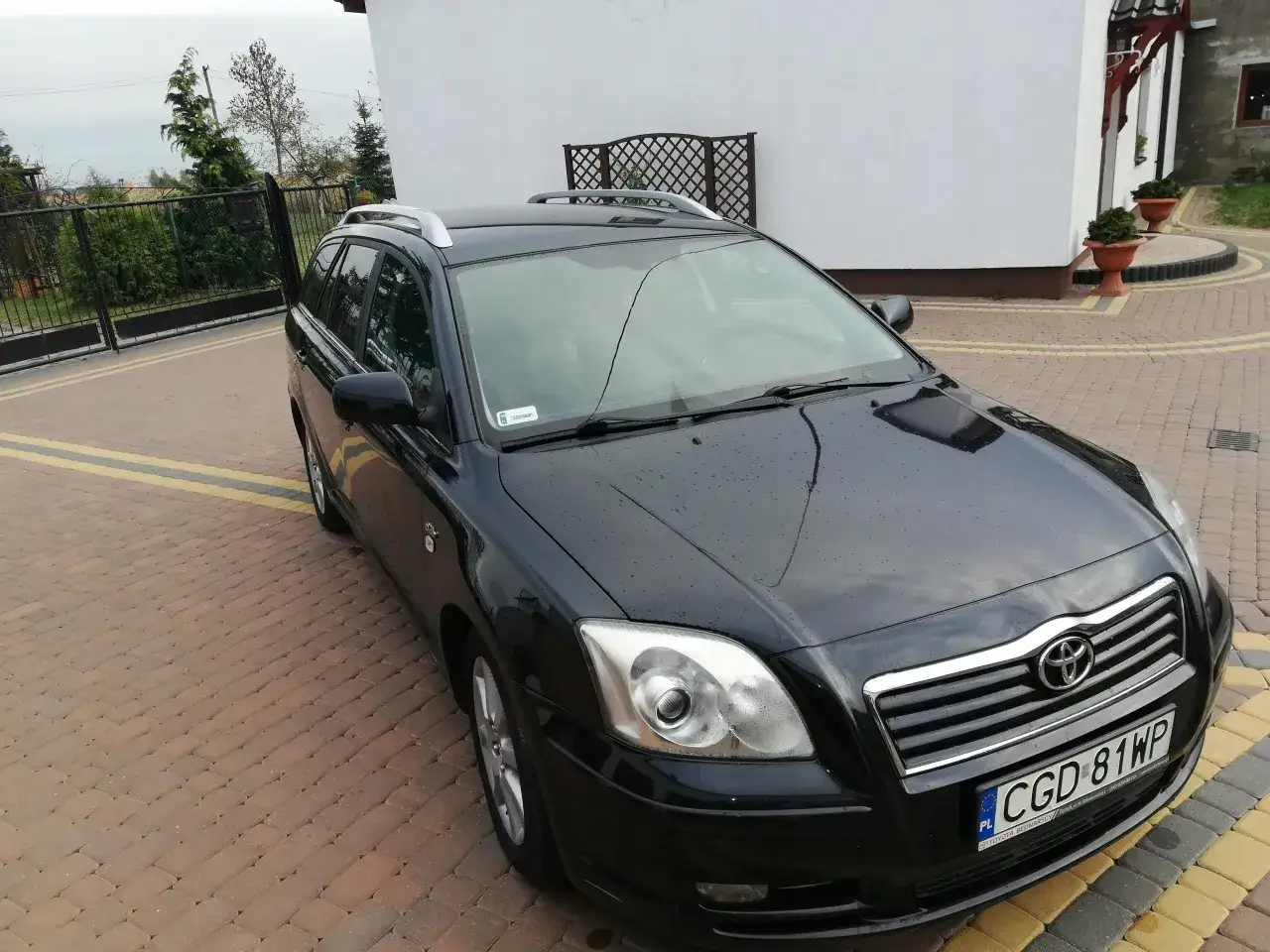 Czarna Toyota Avensis 2.0 D4D na podjeździe z kostki brukowej, z widocznym numerem rejestracyjnym CGD 81WP.