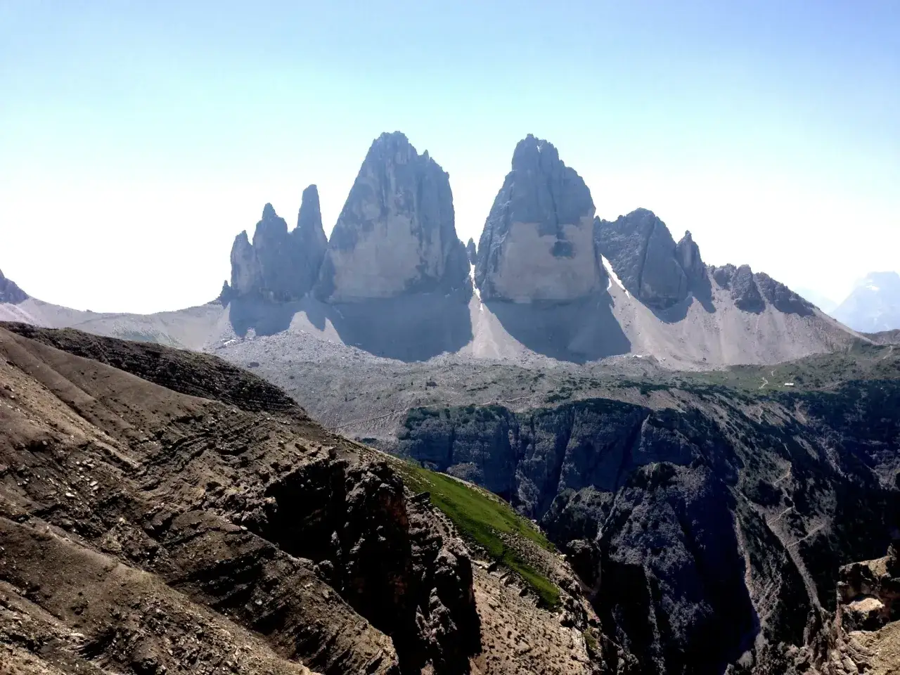 Majestätisches Gebirge in Italien, die Drei Zinnen ragen imposant in den blauen Himmel. Ein Wanderweg schlängelt sich durch die felsige Landschaft.
