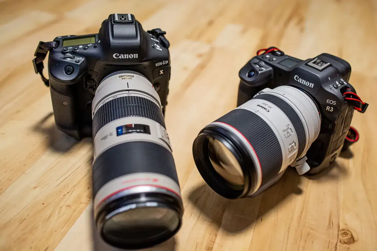 Dwa aparaty Canon: EOS-1D X z obiektywem 70-200 mm i EOS R3 z obiektywem 70-200 mm, leżą na drewnianym blacie.