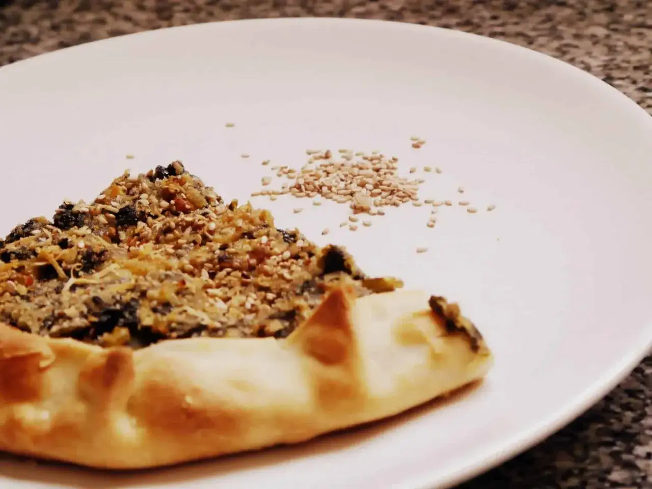 Un trozo de pastel de acelgas con semillas de s&eacute;samo espolvoreadas sobre un plato blanco.