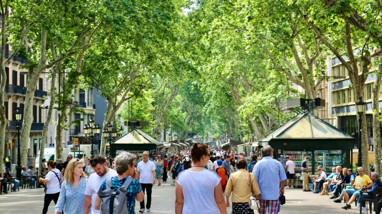 Gente pasea por una calle arbolada con puestos, un ejemplo de negocios rentables en un pueblo.
