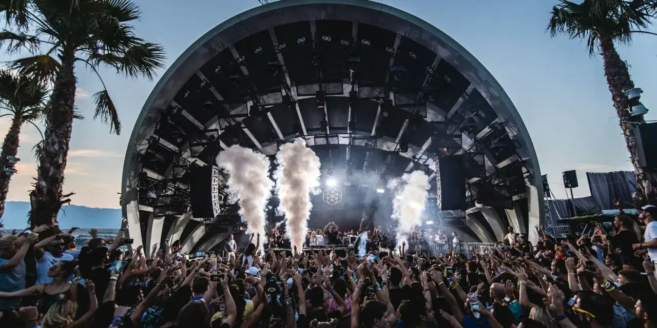 Folla in delirio sotto una grande struttura da concerto, con fumo e luci che creano un'atmosfera perfetta per la musica tech house.