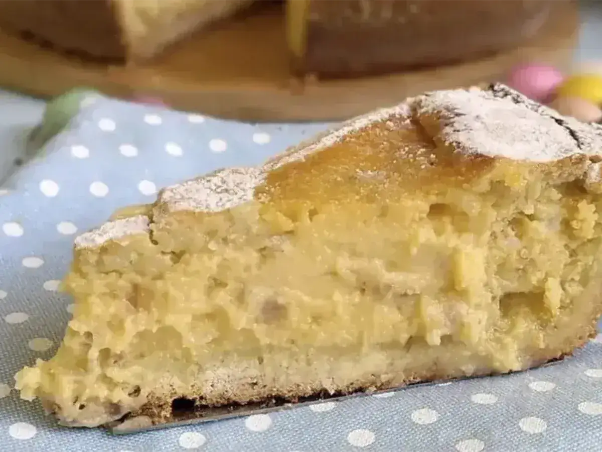 Una fetta di pastiera napoletana con crema pasticcera, cosparsa di zucchero a velo, su un tovagliolo a pois azzurri.