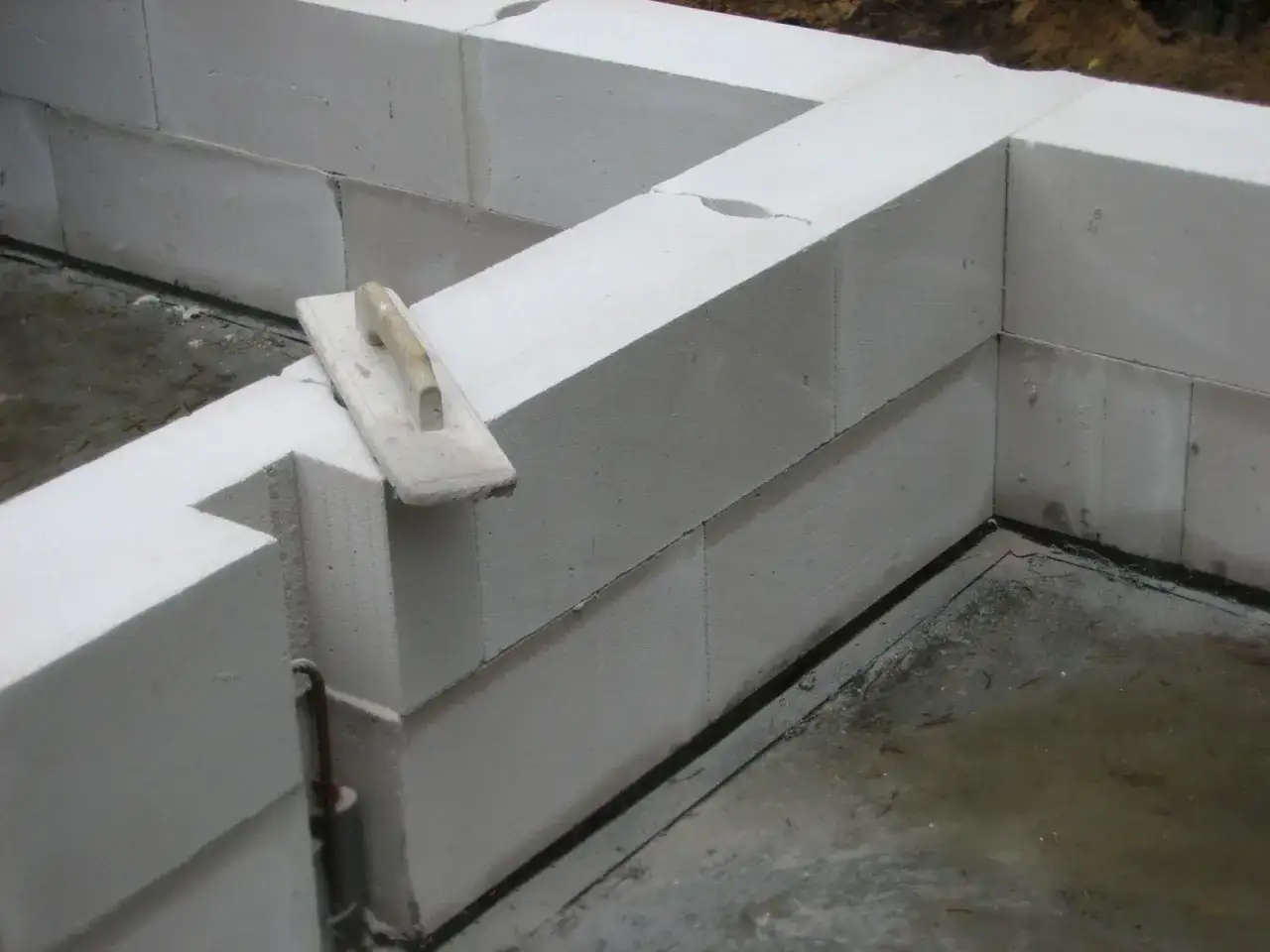 Murowanie ścian z bloczków betonowych. Sprawdź murowanie ścian cena za m2 robocizna. Na zdjęciu kielnia i budowane fundamenty.