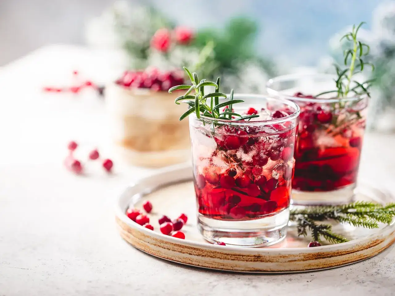 Zwei erfrischende Silvester Cocktails mit Gin, Cranberries und Rosmarin auf einem festlichen Teller.