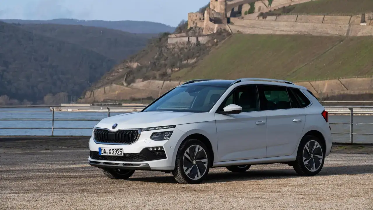 Biały Skoda Kamiq z czarnym dachem stoi na żwirowym podjeździe. W tle rzeka, wzgórza i ruiny zamku.
