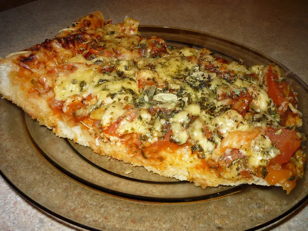 Pyszna pizza bez mięsa, z ciągnącym się serem, pomidorami i ziołami, podana na szklanym talerzu.