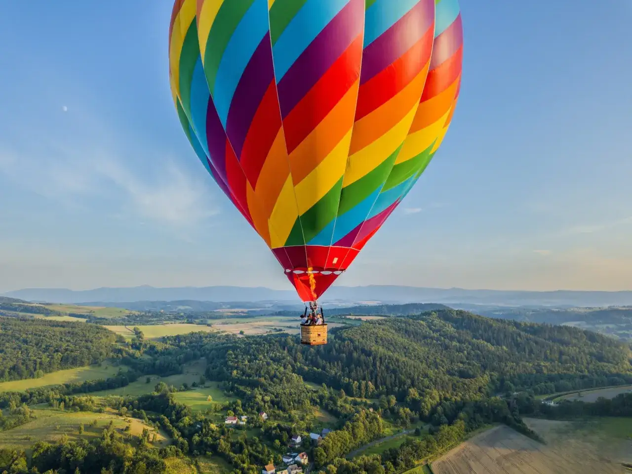 Kolorowy balon unosi się nad zielonymi wzgórzami. Zastanawiasz się, ile kosztuje lot balonem? To niezapomniane przeżycie!