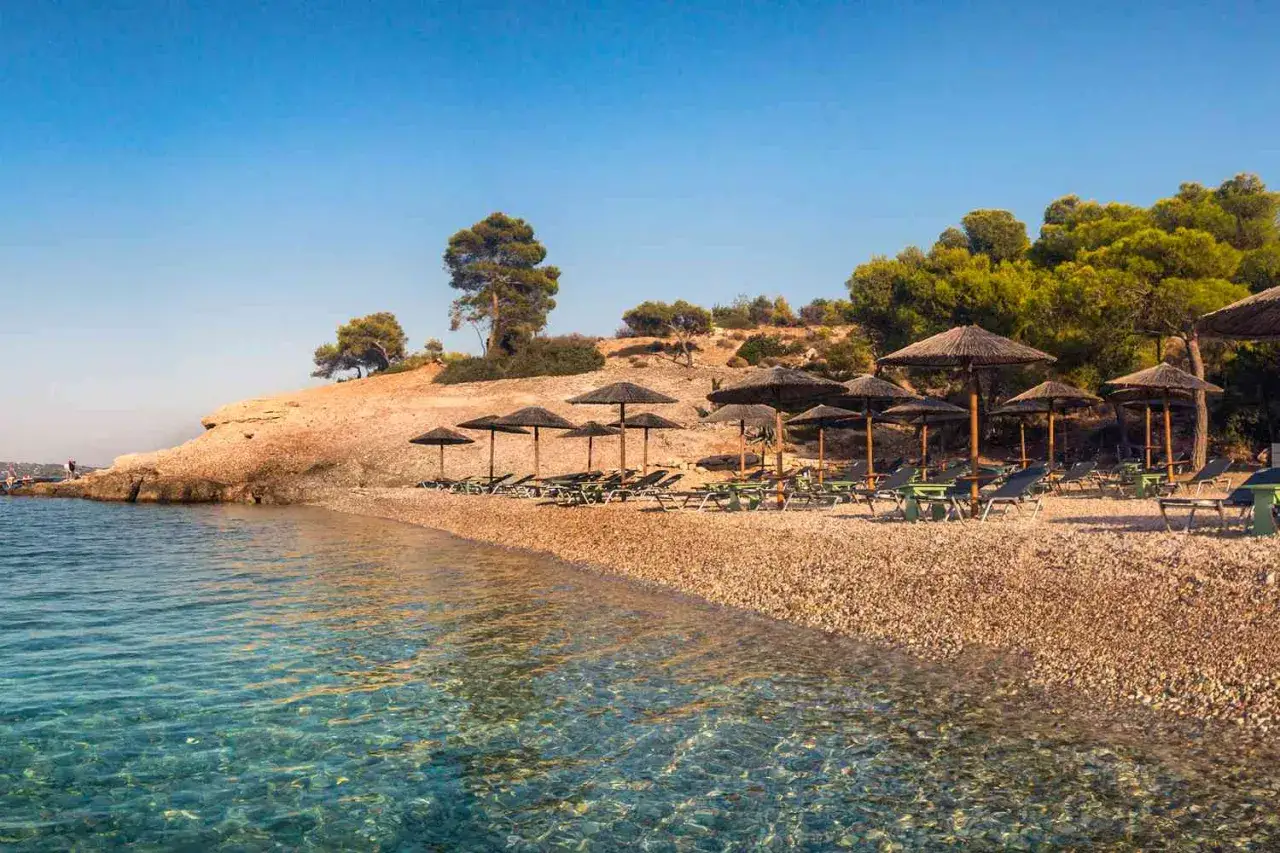 Kamienista plaża z leżakami i parasolami, turkusowa woda. Czy to Rodos czy Kreta?