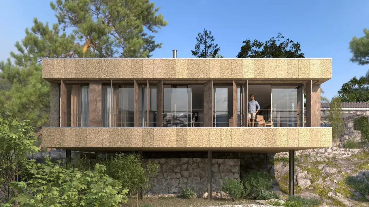 Un hombre disfruta de la vista desde el balc&oacute;n de unas casas de campo modernas, rodeadas de vegetaci&oacute;n y rocas.
