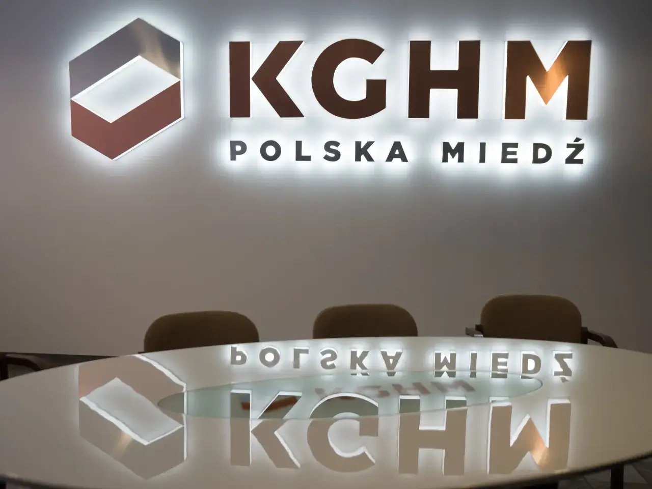 Logo KGHM Polska Miedź i odbicie w stole konferencyjnym. Kto zyska najwięcej na obniżeniu podatku miedziowego od wydobycia kopalin?