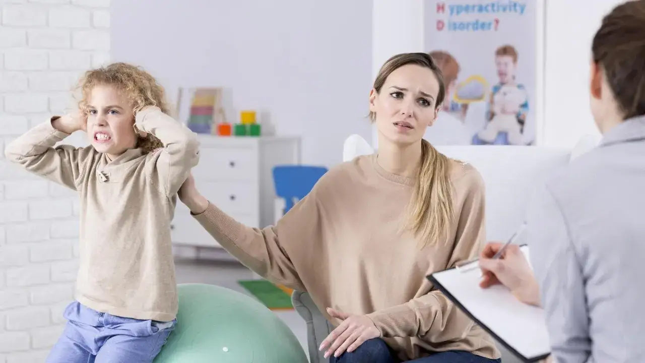 Besorgte Mutter teilt ihre Erfahrungen mit Ritalin bei Kindern mit einem Therapeuten, während ihr Sohn frustriert die Ohren zuhält.