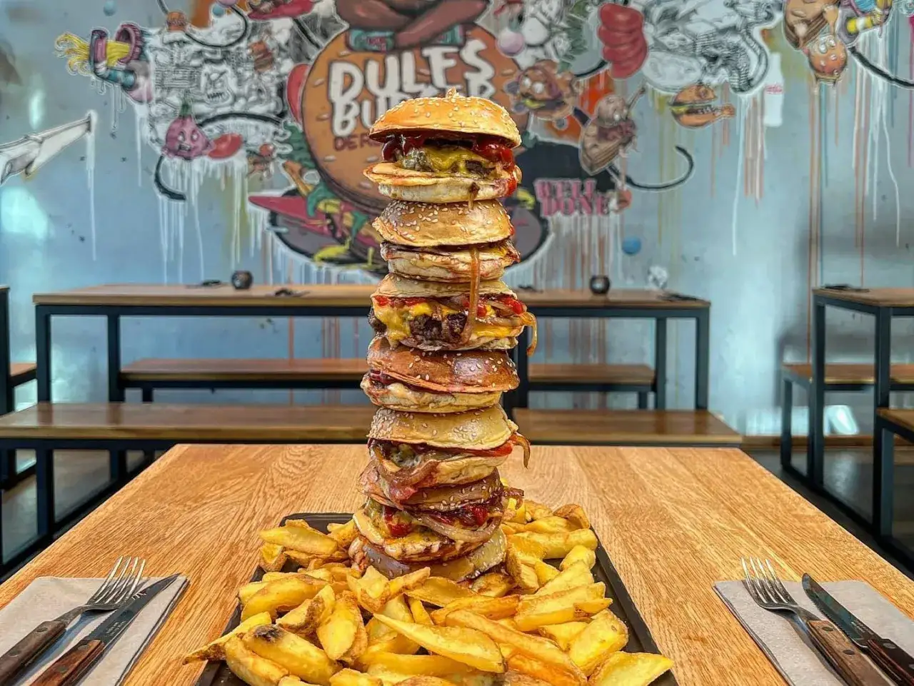 Gigantischer Turm aus Burgern im Dulfs Burger Laden Berlin, serviert mit knusprigen Pommes.