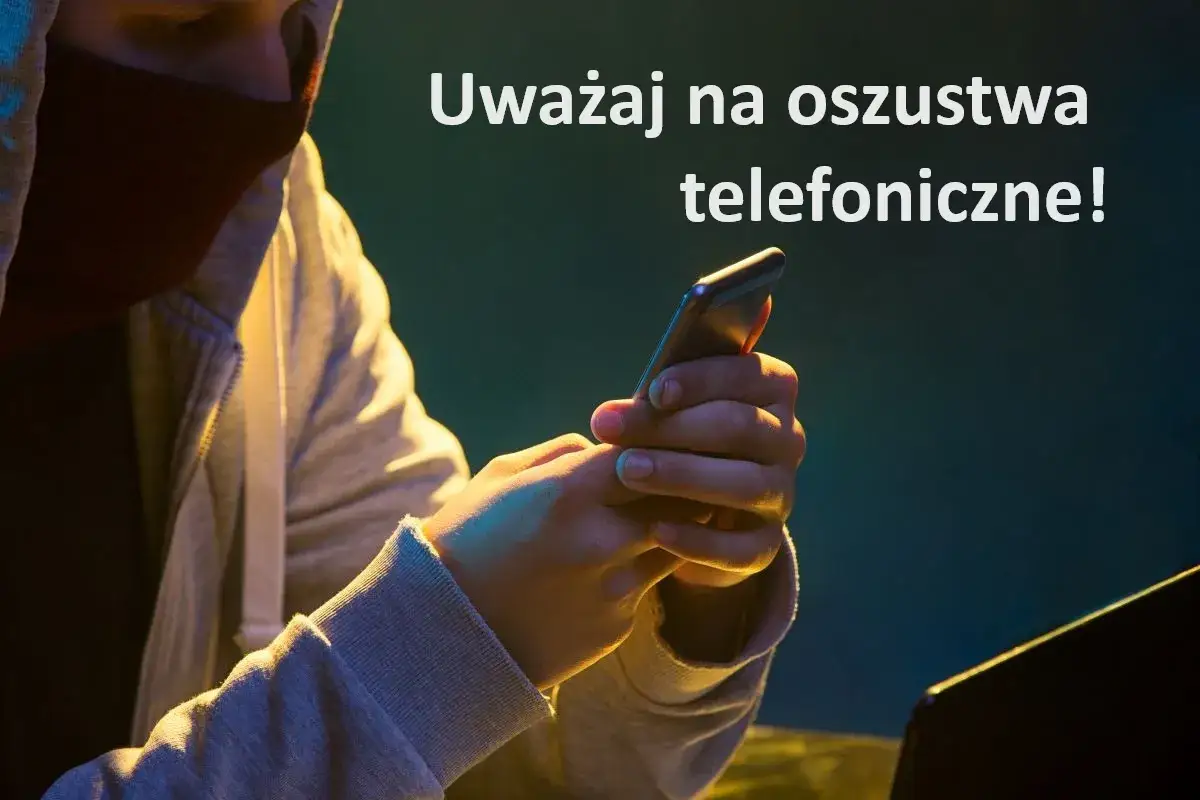 Osoba w kapturze trzyma smartfon, ostrzegając przed oszustwami telefonicznymi. Uważaj na vishing!